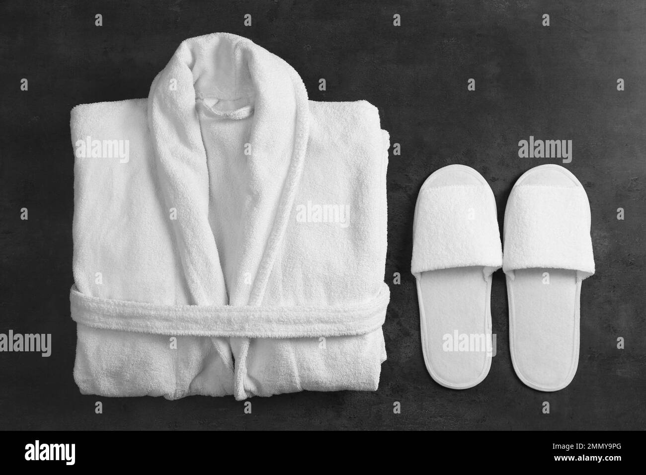 Gefaltete Bademantel und Hausschuhe auf schwarzem Steinhintergrund reinigen, flach legen Stockfoto