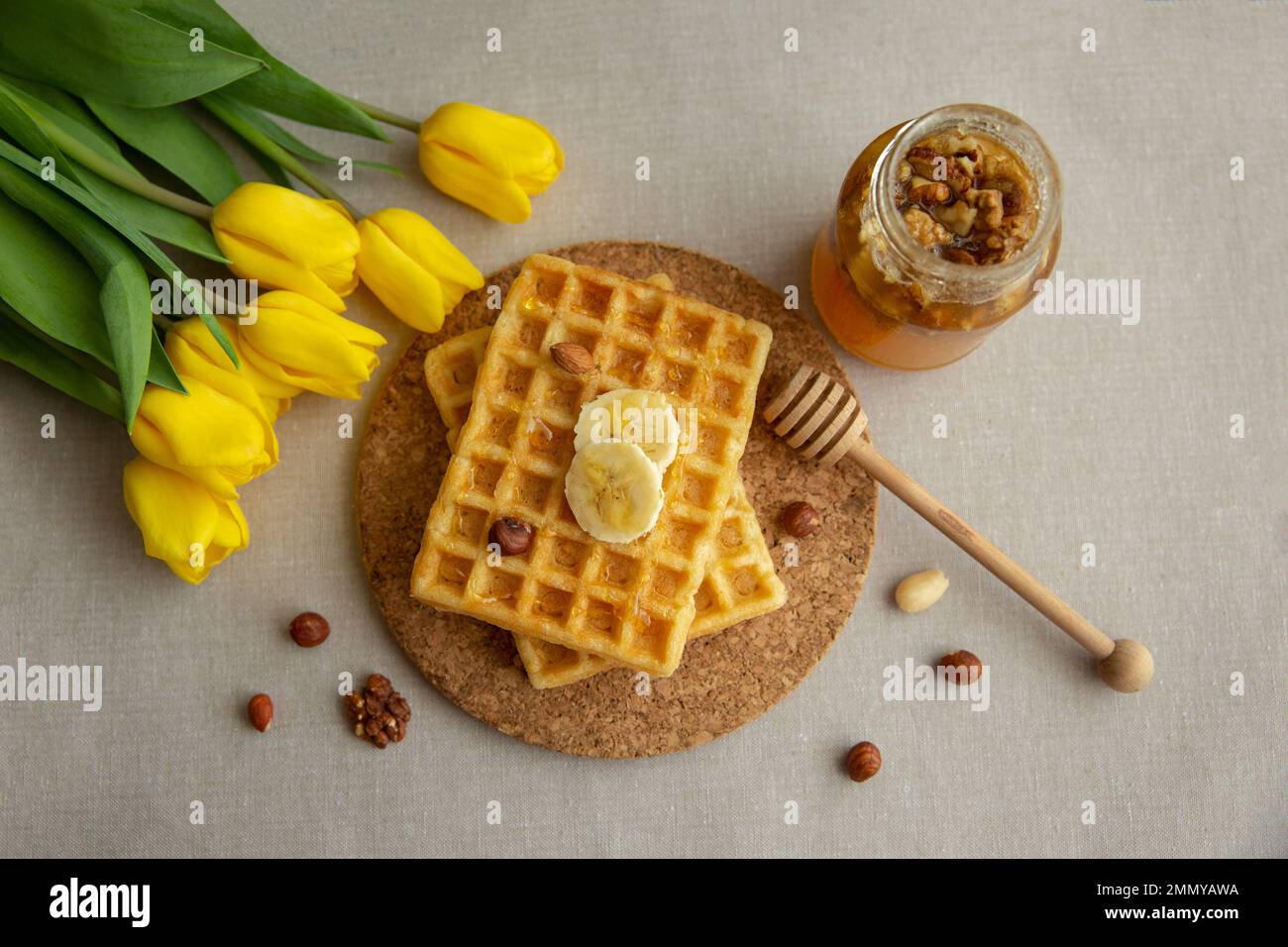 Hausgemachte belgische Waffeln mit Honig, Nüssen und gelben Tulpen Stockfoto