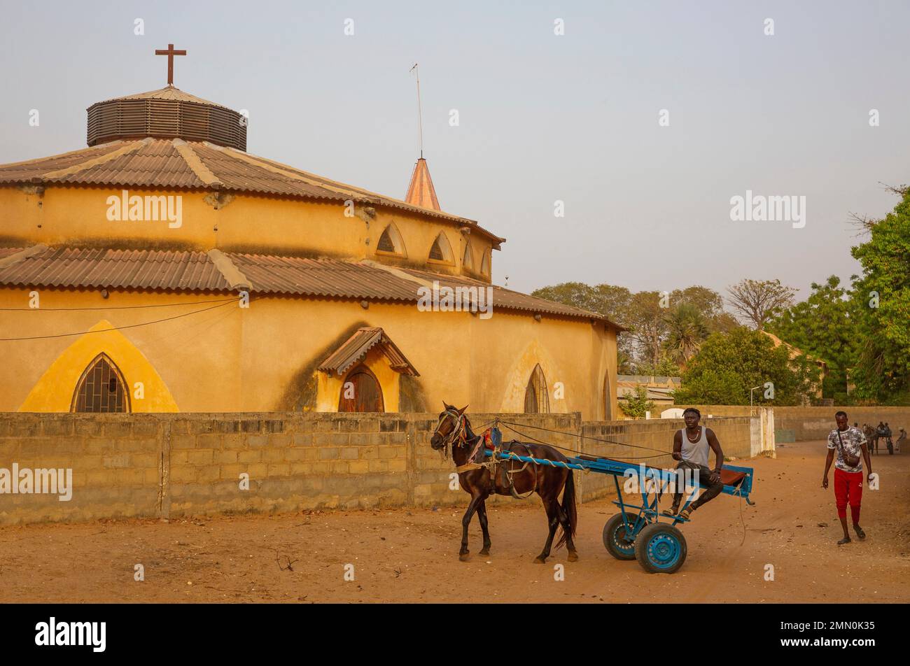 Senegal, Saloum Delta, das von der UNESCO zum Weltkulturerbe erklärt wurde, junger Mann, der einen Pferdewagen vor der Ocker Kirche der Heiligen Familie auf der Insel Mar Lodj fährt Stockfoto