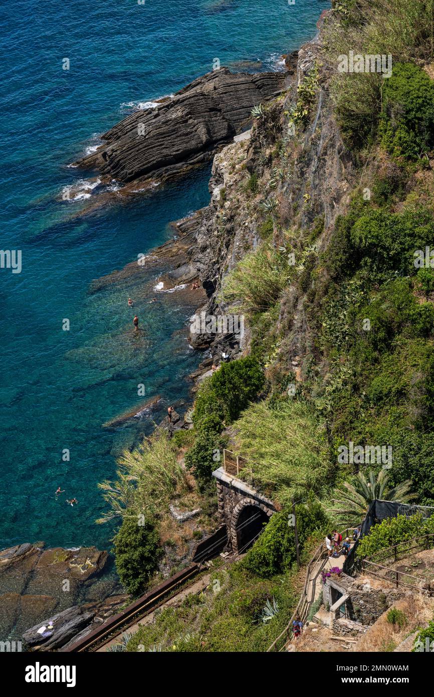 Italien, Ligurien, Nationalpark Cinque Terre, UNESCO-Weltkulturerbe, Dorf Vernazza, Wanderer auf dem GR 592 Küstenpfad mit Blick auf die Bahnlinie und Schwimmer am Fuße der Klippen Stockfoto