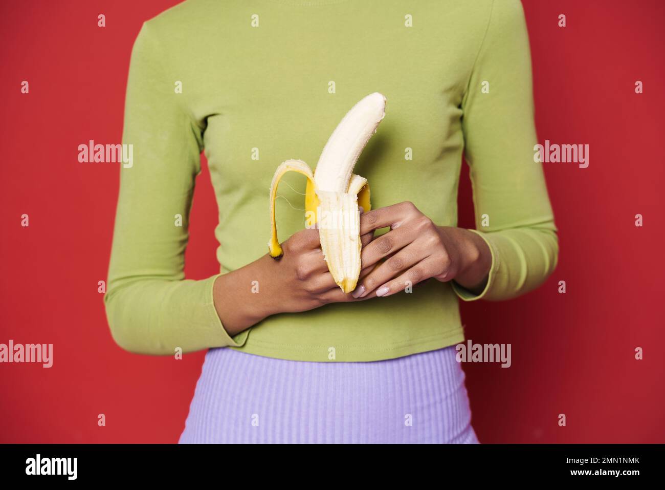 Junge schwarze Frau in grünem Pullover mit isolierter Banane auf rotem Hintergrund Stockfoto
