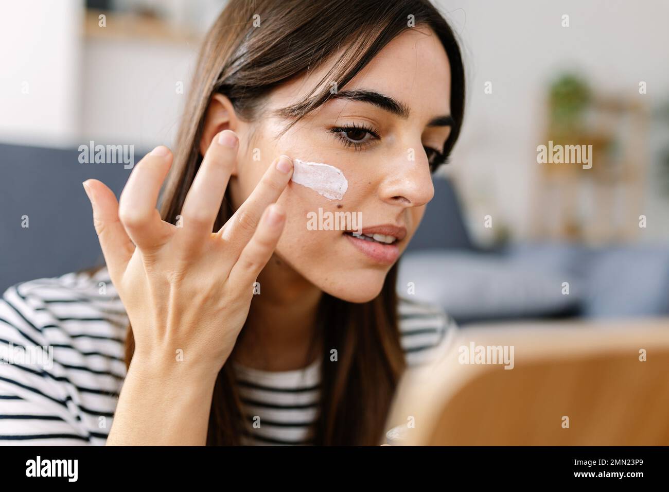 Junge Frau, die Hautpflegeprodukte verwendet. Frau, die Creme zur Anwendung auf die Gesichtshaut einnimmt Stockfoto
