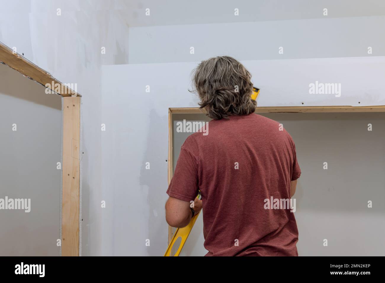 Arbeiter, die eine Hilfsstufe verwenden, prüfen den Füllstand von Trockenbauwänden vor dem Lackieren, um sicherzustellen, dass er gleich ist Stockfoto