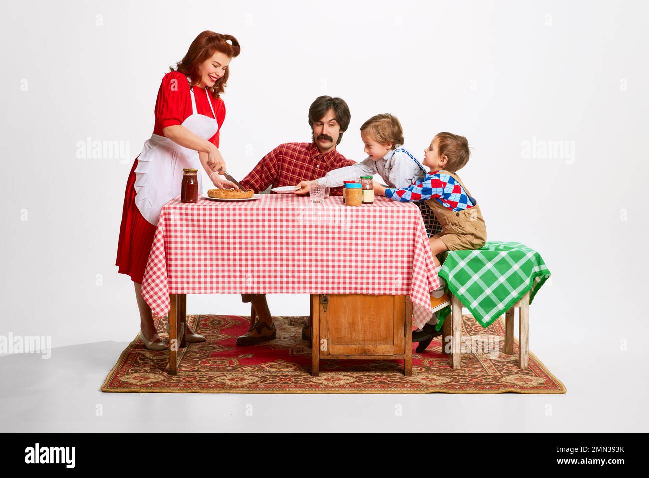 Lauter schöner Familienvormittag. Schöne Frau, die ihrem Mann und ihren Söhnen Kuchen servierte, die am Küchentisch saßen Stockfoto