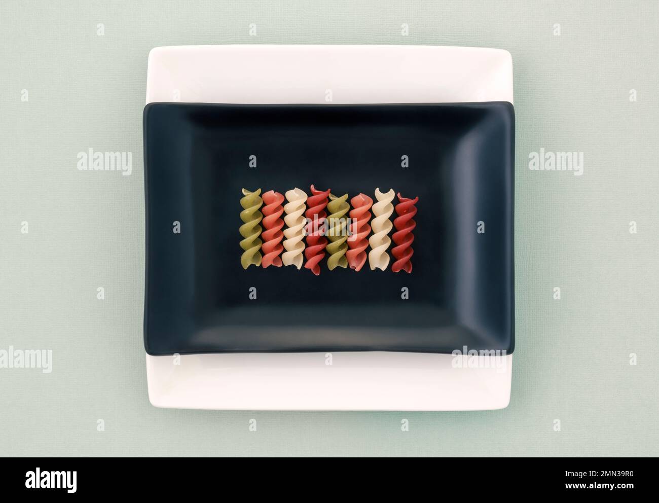 Spiralen mit Gemüse-Reis-Pasta, die in einer Linie auf einer schwarzen quadratischen Schüssel angeordnet sind Stockfoto