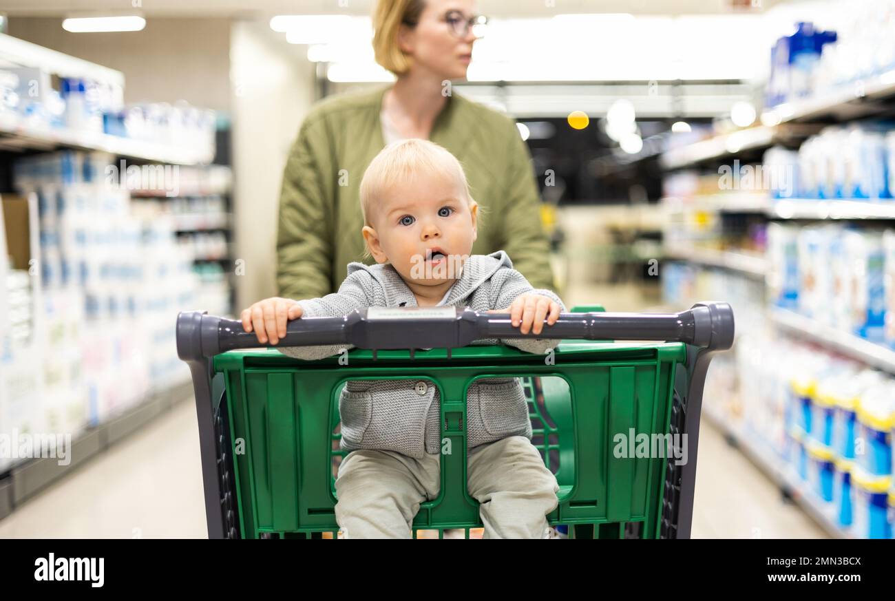 Mutter schiebt den Einkaufswagen mit ihrem kleinen Jungen durch die Abteilung im Supermarkt. Einkaufen mit Kindern Konzept Stockfoto