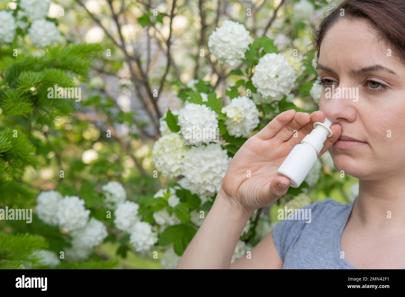 Kaukasische Frau verwendet ein Nasenspray, während sie im Park spazieren geht. Stockfoto