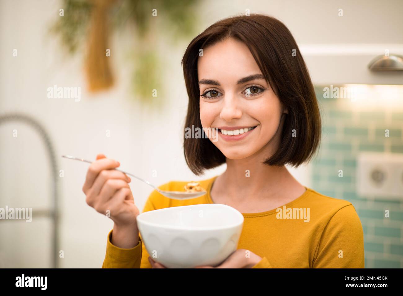 Nahaufnahme einer fröhlichen jungen Frau, die zu Hause Frühstückscerealien isst Stockfoto