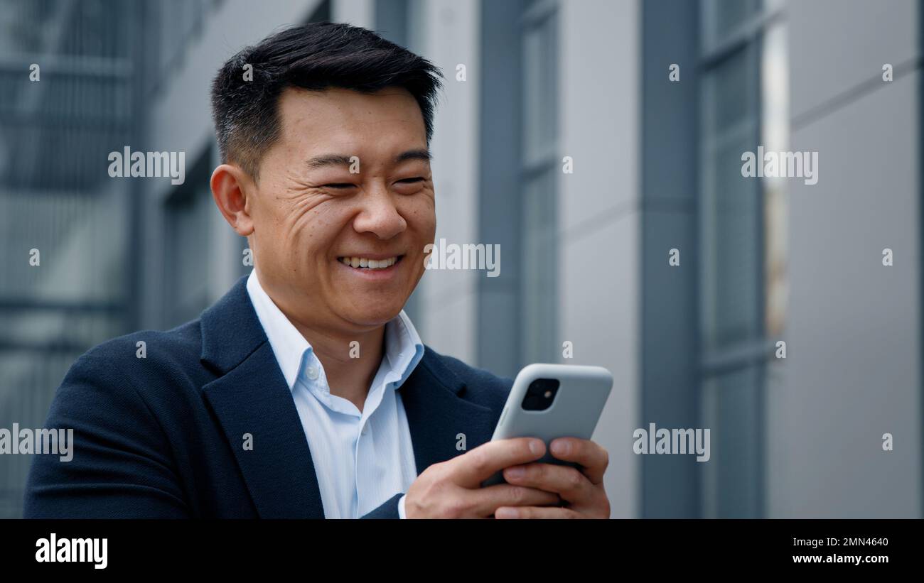 Emotionales Lächeln Asiens im mittleren Alter koreanischer Geschäftsmann Arbeitgeber Unternehmer lacht, wenn er auf ein Mobiltelefon schaut, sich chattet und lächelt Stockfoto