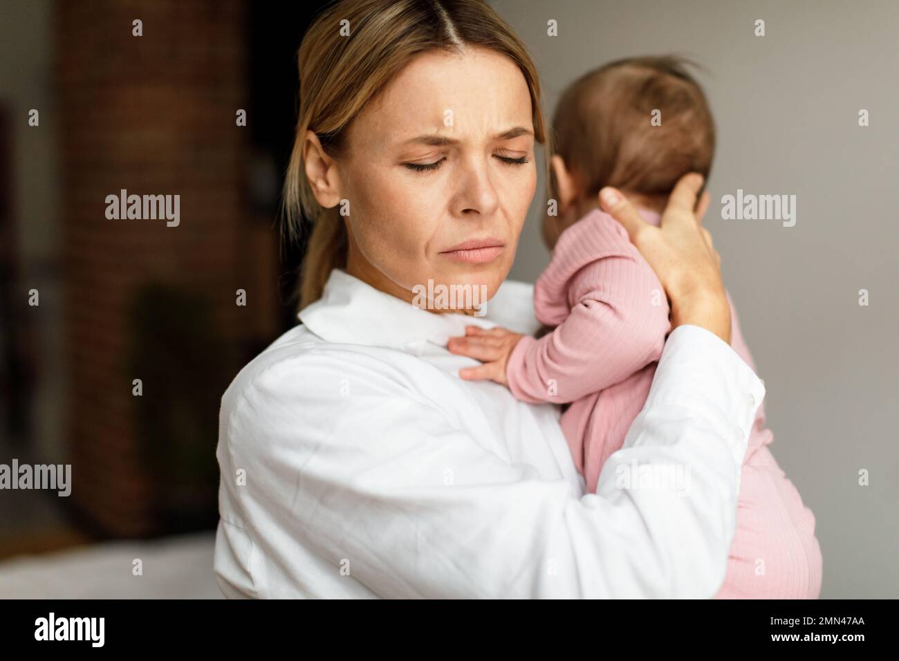 Erschöpfte Mutter, die ein kleines Baby hält, im Schlafzimmer zu Hause steht, Kopierraum Stockfoto