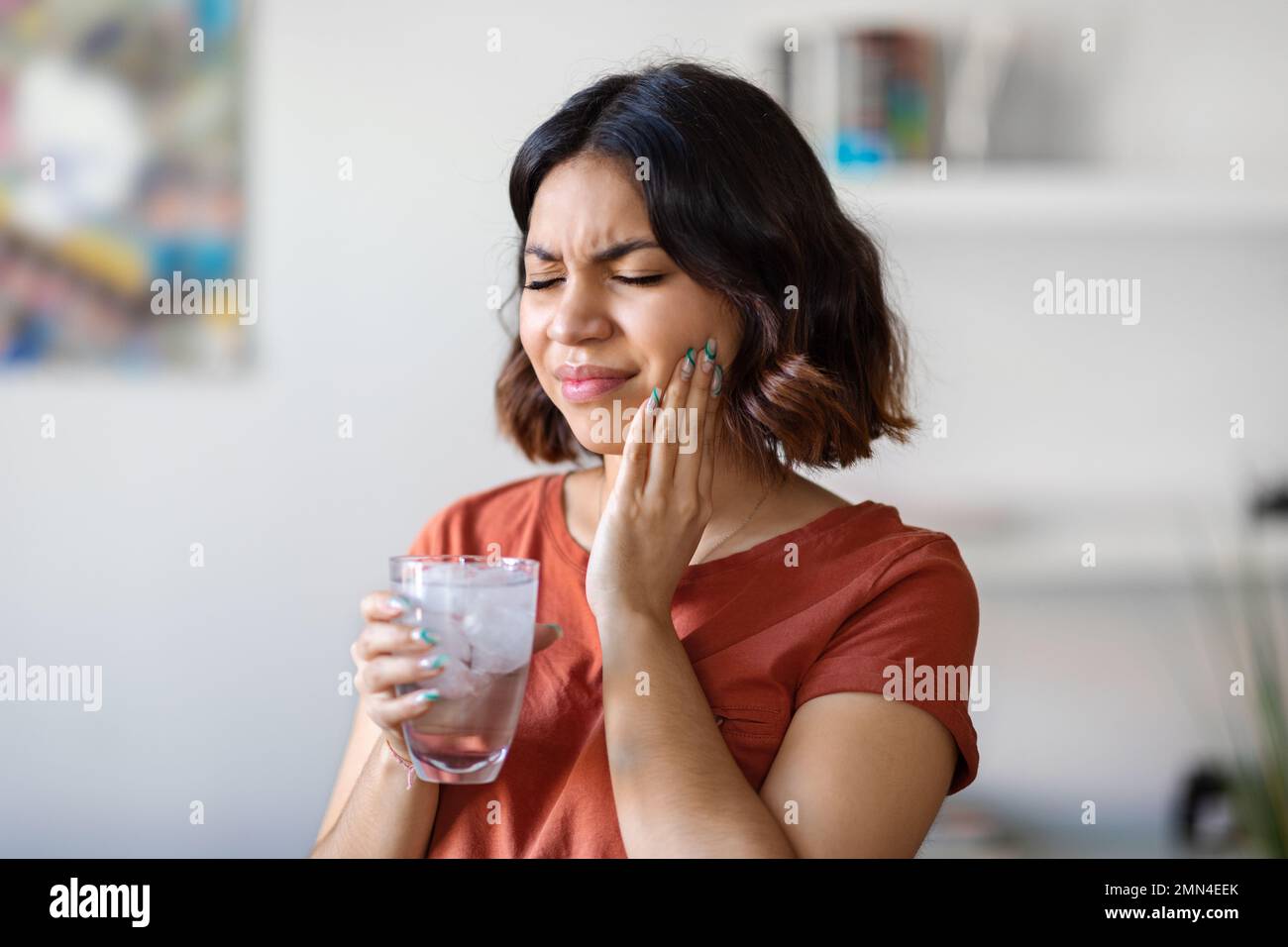 Empfindliche Zähne. Junge araberin trinkt Wasser mit Eis und berührt die Wange Stockfoto
