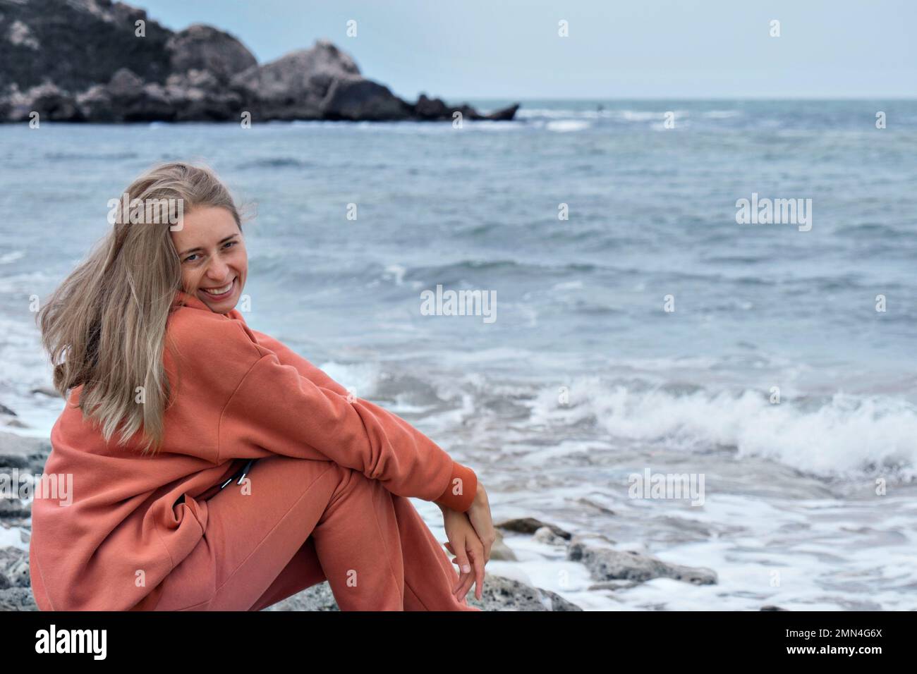 Ein Mädchen mit europäischem Aussehen und langen braunen Haaren sitzt am Meer und genießt einen Moment und einen wunderschönen Blick, betet, meditiert. Ruhen Sie sich auf dem Meer aus. Einsamkeit mit der Natur. Hochwertiges Foto Stockfoto