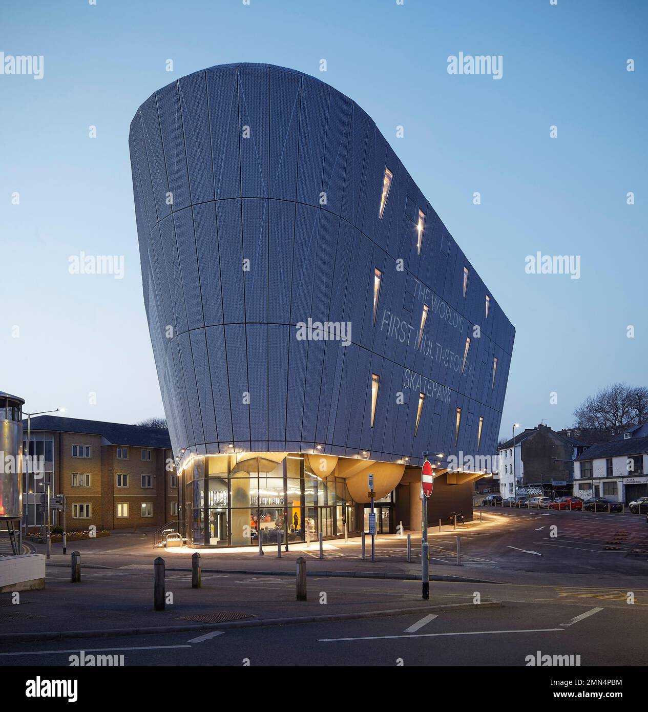 Blick in die Abenddämmerung auf der anderen Straßenseite in Richtung Skatepark mit Aluminiumgitterverkleidung. F51 Skatepark, Folkestone, Vereinigtes Königreich. Architekt: Hollaway Studio, 2022. Stockfoto