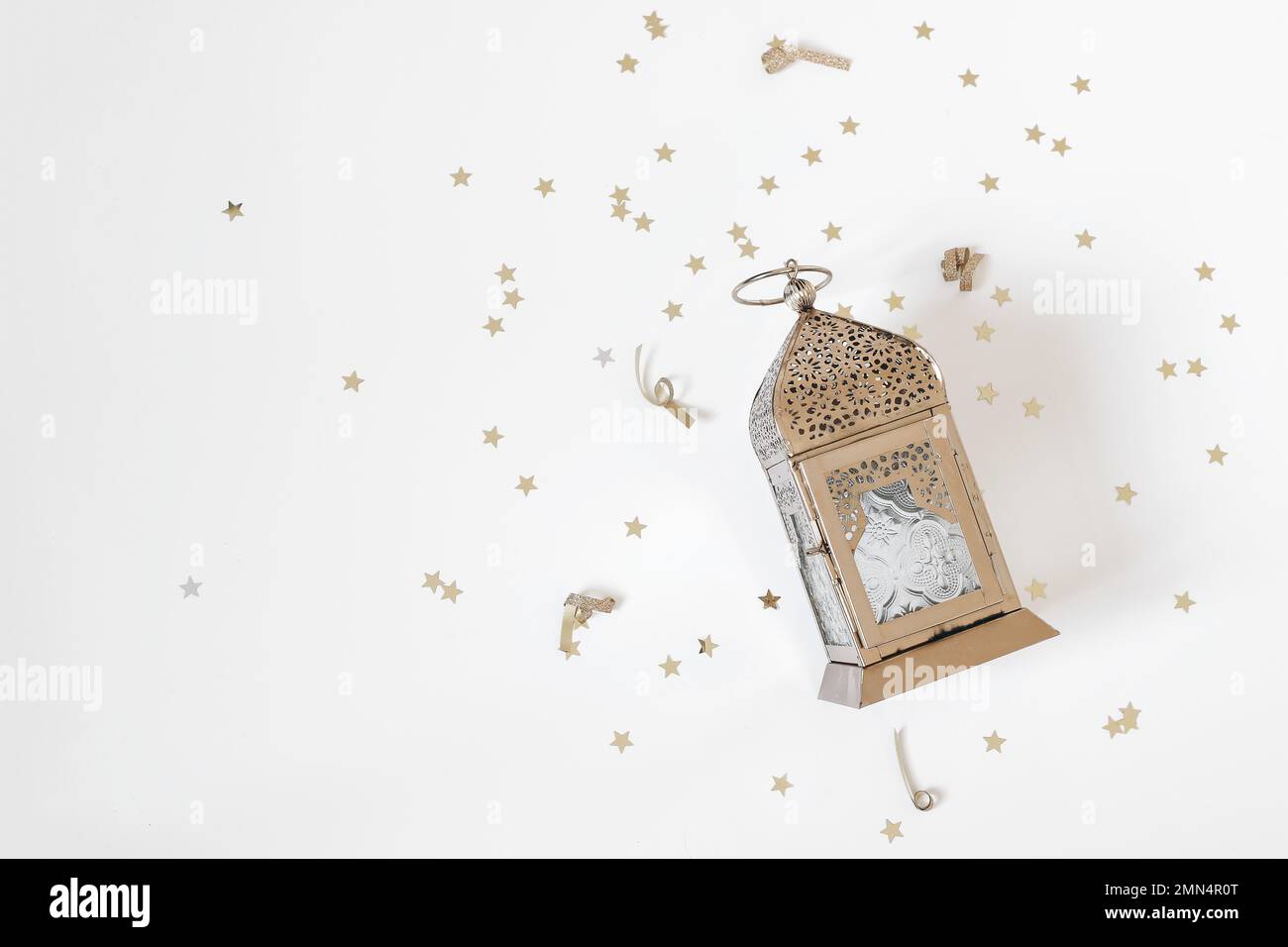 Festliche Ramadan-Weihnachtskomposition, Webbanner. Goldene dekorative marokkanische Laterne und sternförmige Konfetti isoliert auf weißem Tischhintergrund. Iftar Stockfoto