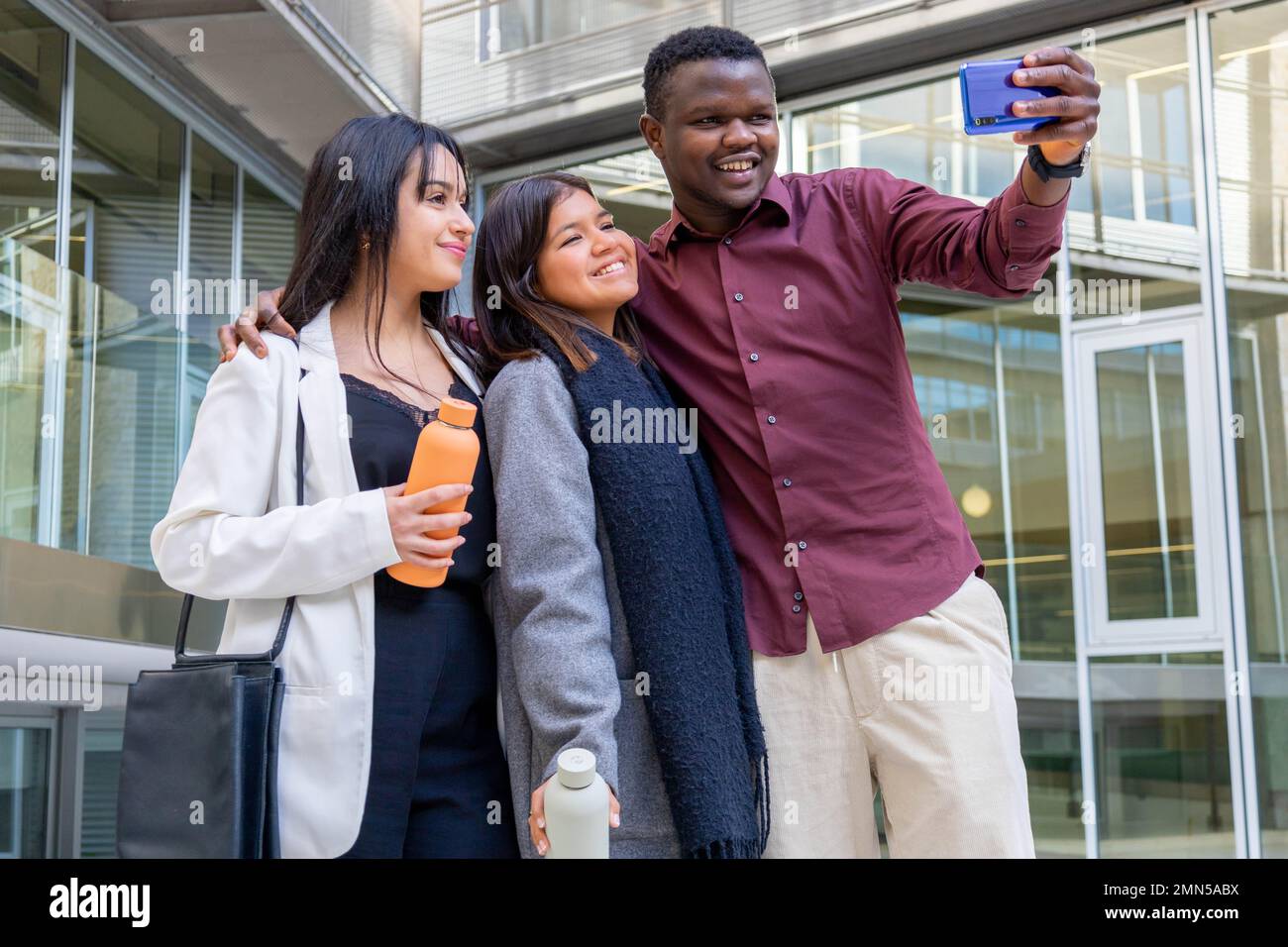 Attraktive Kollegen machen ein Selfie mit einem Smartphone außerhalb des Büros. Gruppe von Freunden, die in der Arbeitspause lächeln. Ethnische Vielfalt, soziale Eingliederung. Stockfoto