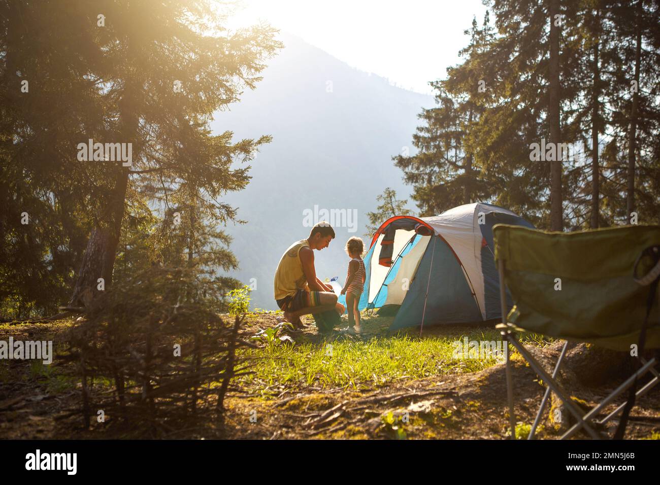 Vater und Tochter im Alter von 2 Jahren in der Nähe eines Zelts in einem Camping im Wald in den Bergen. Freizeitaktivitäten für die ganze Familie, umweltfreundliche Abenteuer, Survival i Stockfoto