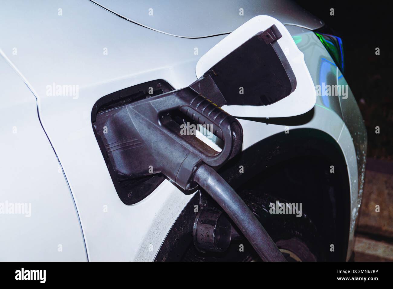 Das weiße Auto ist nachts mit Neonlichtern an die elektrische Ladestation angeschlossen. Stockfoto