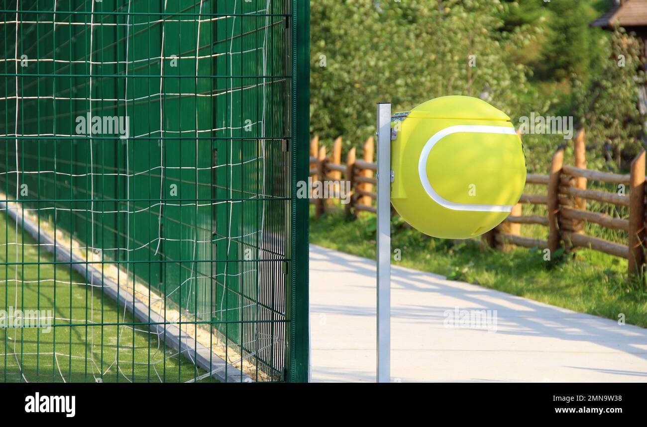 Runder Mülleimer in Form eines Tennisballs in der Nähe eines umzäunten Tennisplatzes Stockfoto