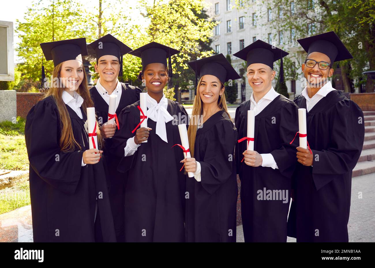 Gruppenporträt von glücklichen, vielfältigen Universitätsschülern in Kappen und Kitteln am Abschlusstag Stockfoto