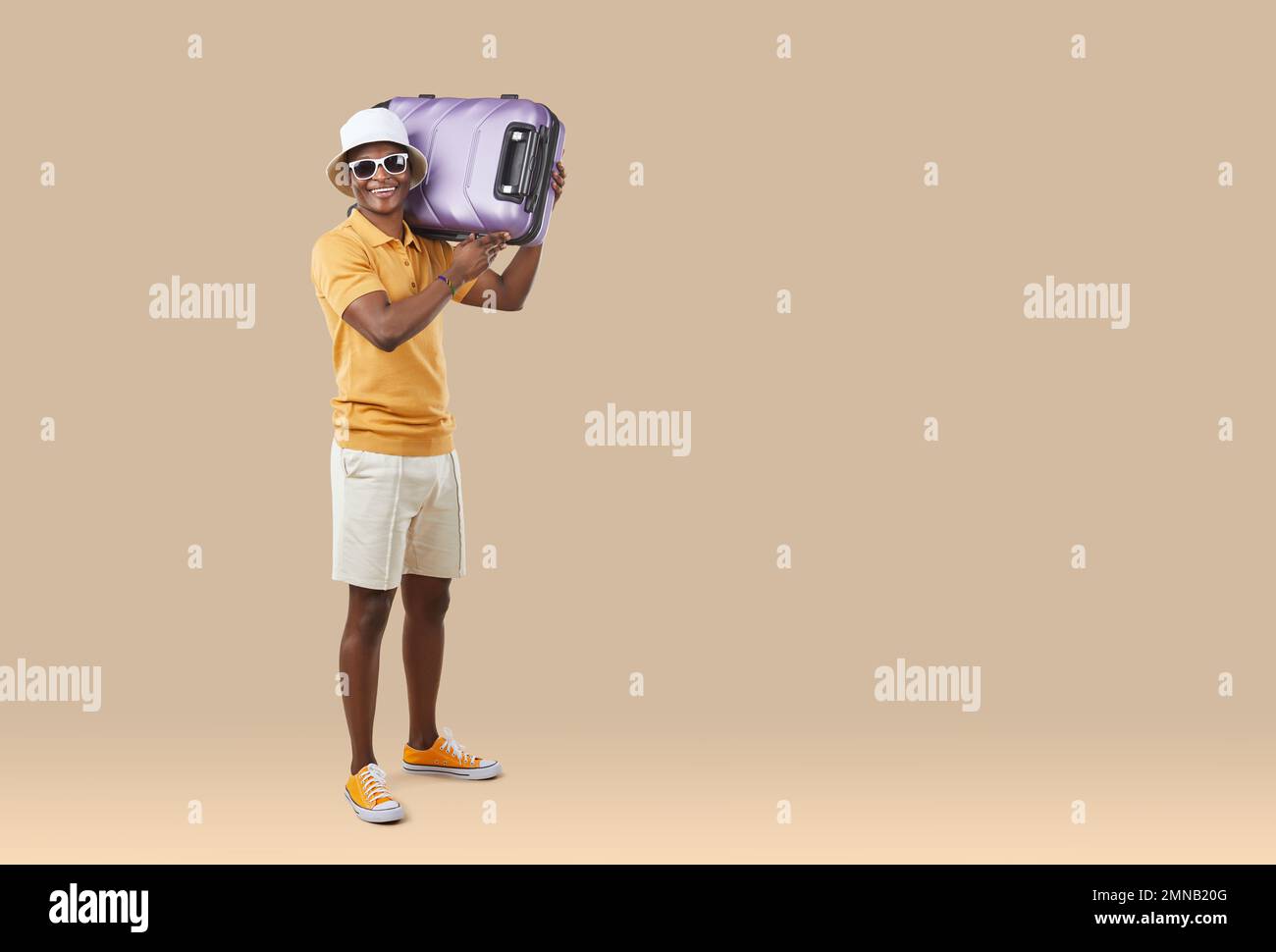 Fröhlicher afroamerikanischer Sommertourist mit Koffer auf den Schultern auf hellem beigefarbenem Hintergrund. Stockfoto