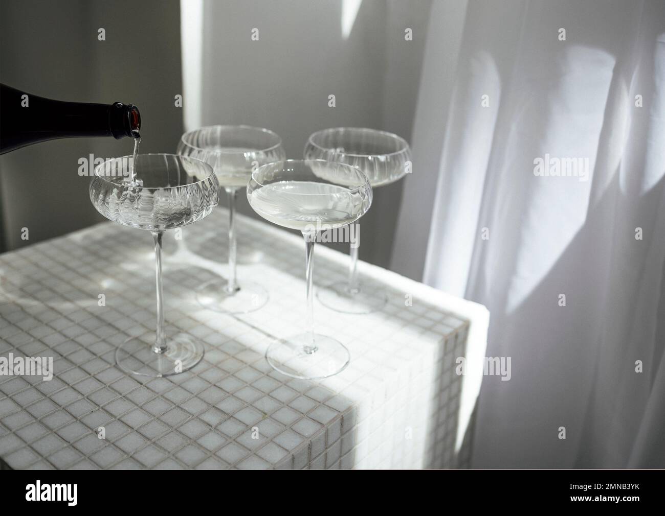 Champagner gießt in Gläser auf einer hellen Tischoberfläche, die den weichen Sonnenschein reflektiert, rayson. Sekt auf der Party Stockfoto