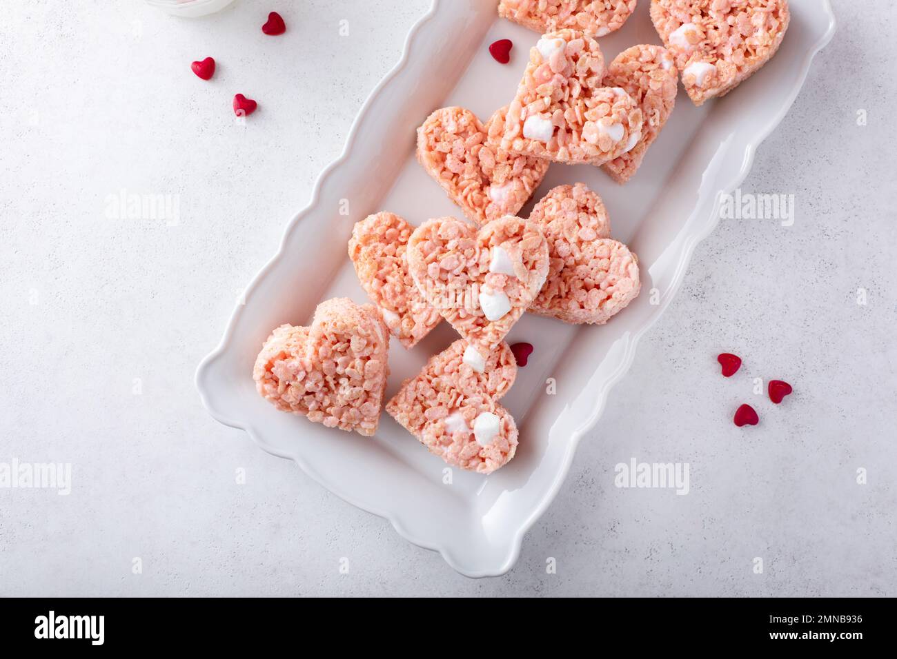 Herzförmige rosafarbene Reiskrispie zum Valentinstag auf einem Teller mit roten Herzstreuseln Stockfoto
