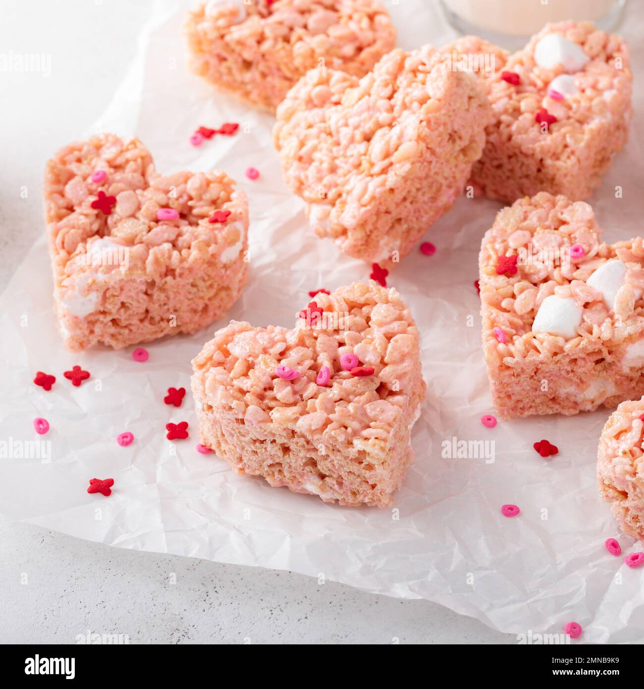 Herzförmige rosafarbene Reiskrispie zum Valentinstag mit roten Herzstreuseln, serviert mit Milch Stockfoto