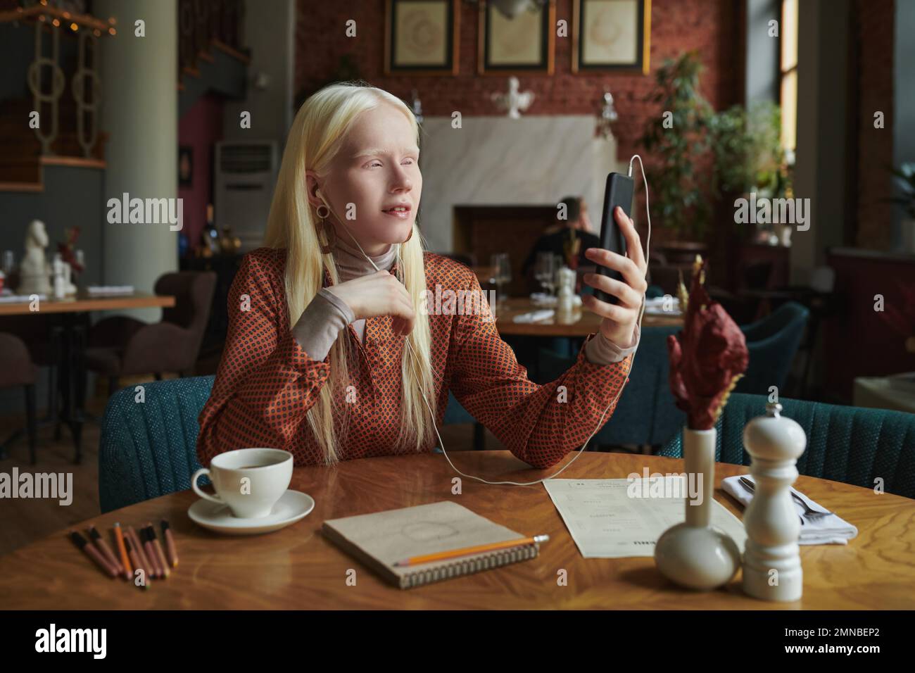 Junge Albino-Frau in Freizeitkleidung, die mit einer Freundin in einem Video-Chat spricht und ihr erklärt, wie sie zum Café gehen kann, wo sie auf sie wartet Stockfoto