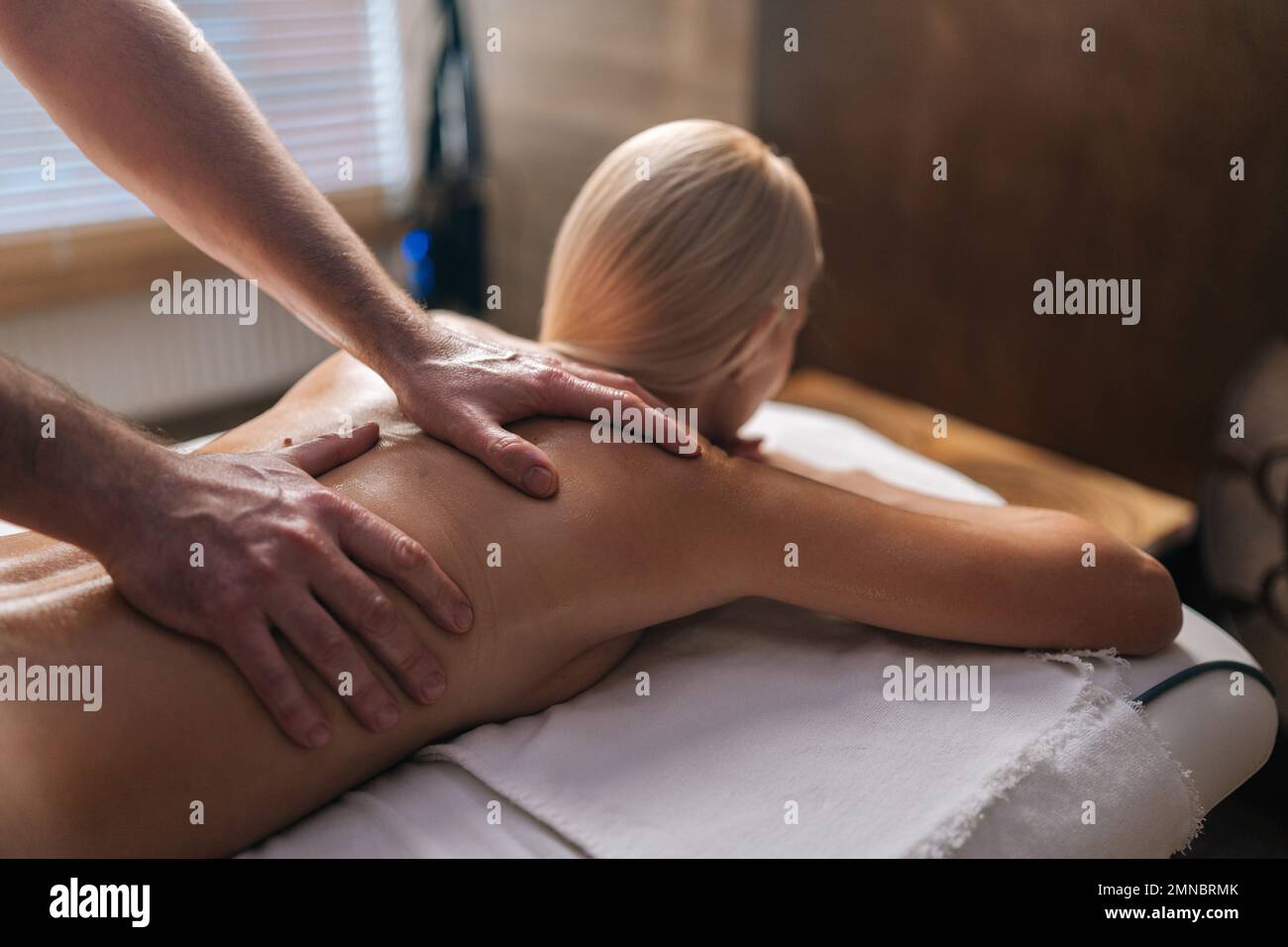 Gekürzte Aufnahme eines nicht wiedererkennbaren männlichen Masseurs, der eine Rückenmassage an eine nackte weibliche Klientin im Spa-Salon auf einem Massagetisch durchführt. Stockfoto
