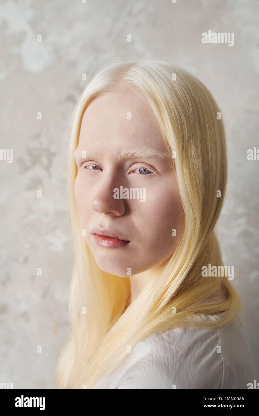 Junge, wunderschöne Albino-Frau ohne Make-up, die auf die Kamera schaut, während sie über die Marmorwand steht und während der Fotosession posiert Stockfoto