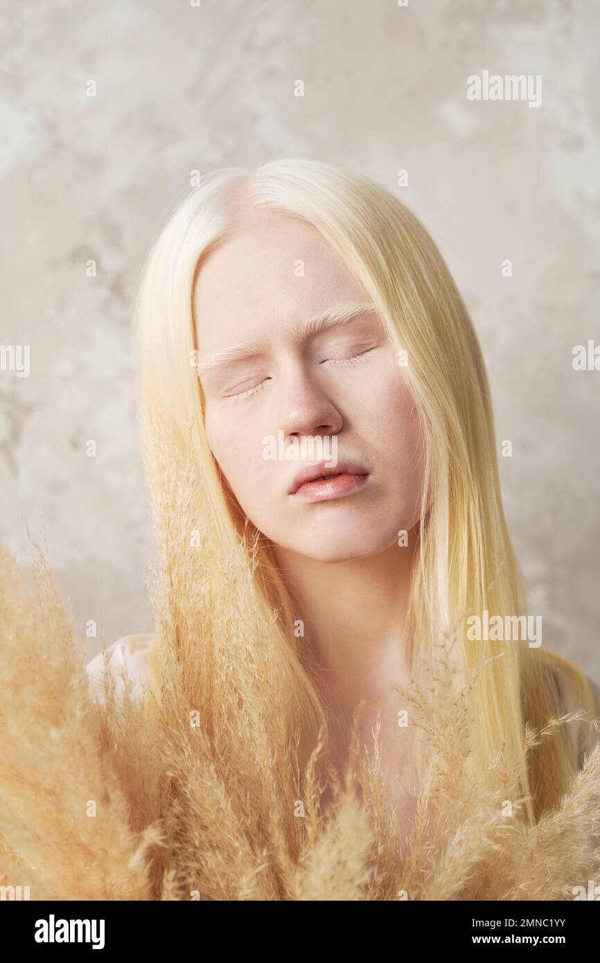 Nahaufnahme des Porträts einer jungen, ruhigen Albino-Frau mit flauschigen, getrockneten Blumen, die die Augen geschlossen halten, während sie isoliert vor der Kamera stehen Stockfoto