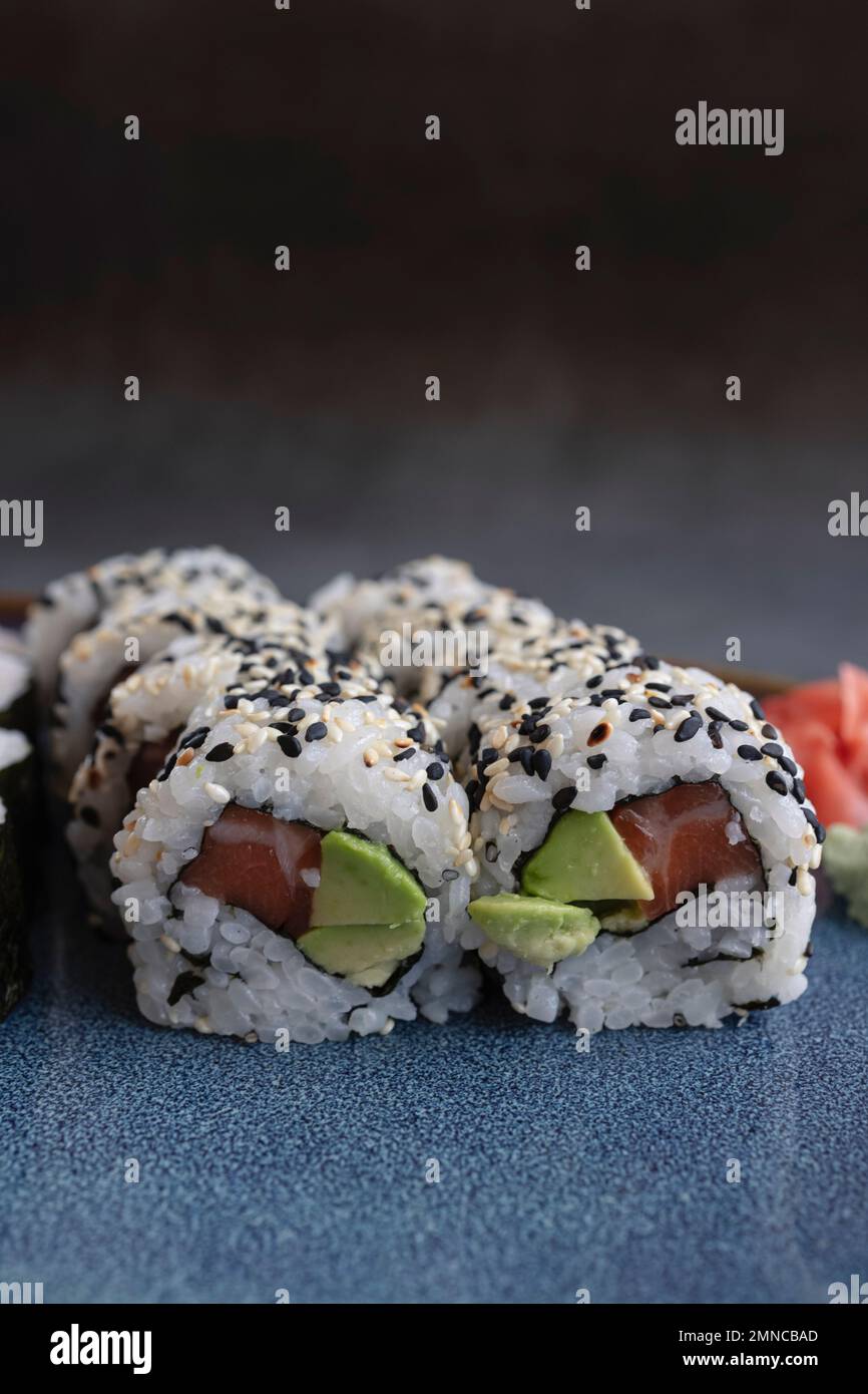 Ein Set frischer Sushi-Brötchen mit Lachs, Avocado und schwarzen Sesamsamen aus nächster Nähe. California Roll, selektive Fokussierung Stockfoto