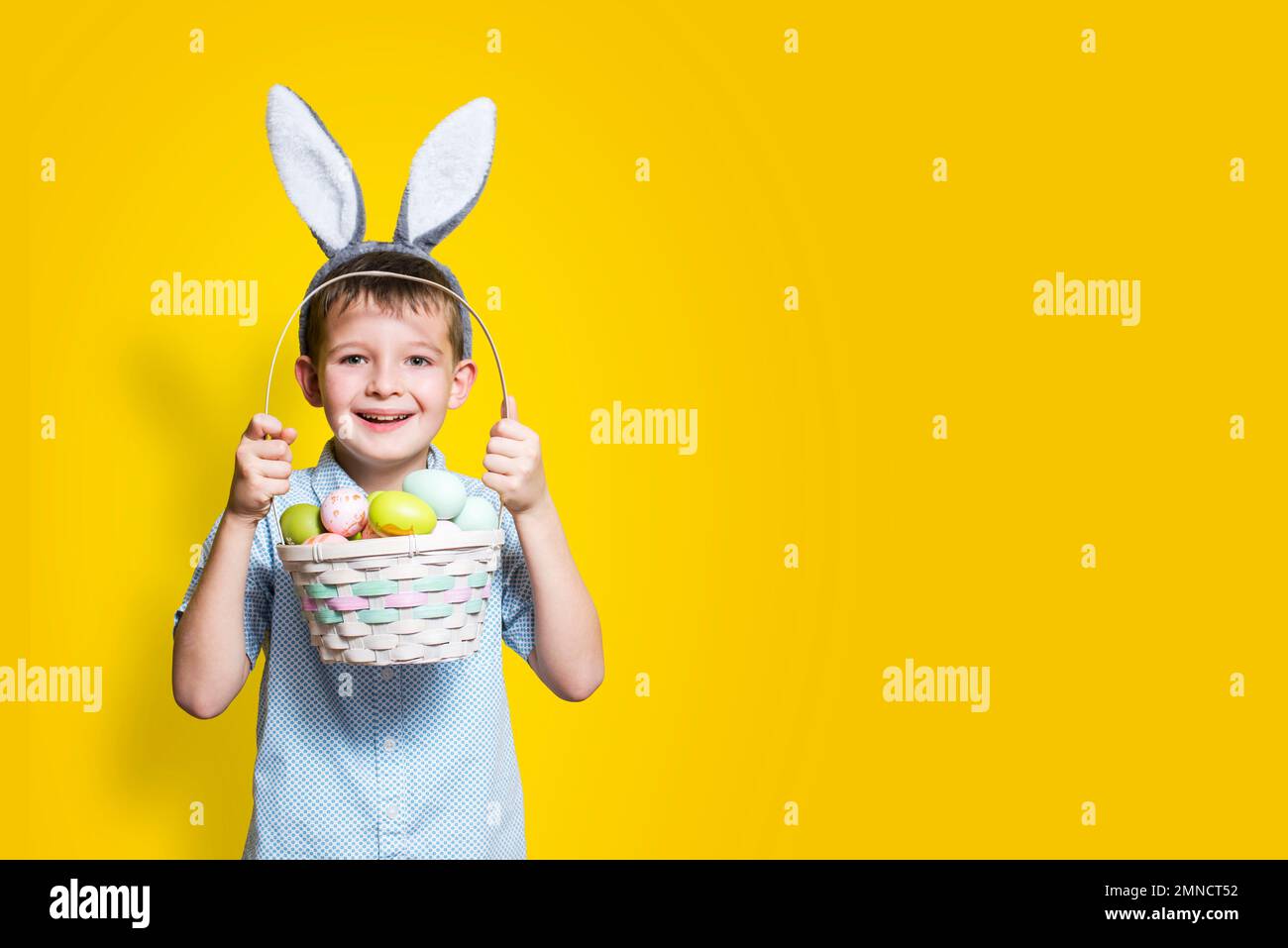 Kleiner süßer Junge mit einem Osterkorb in den Händen und Hasenohren auf dem Kopf Stockfoto