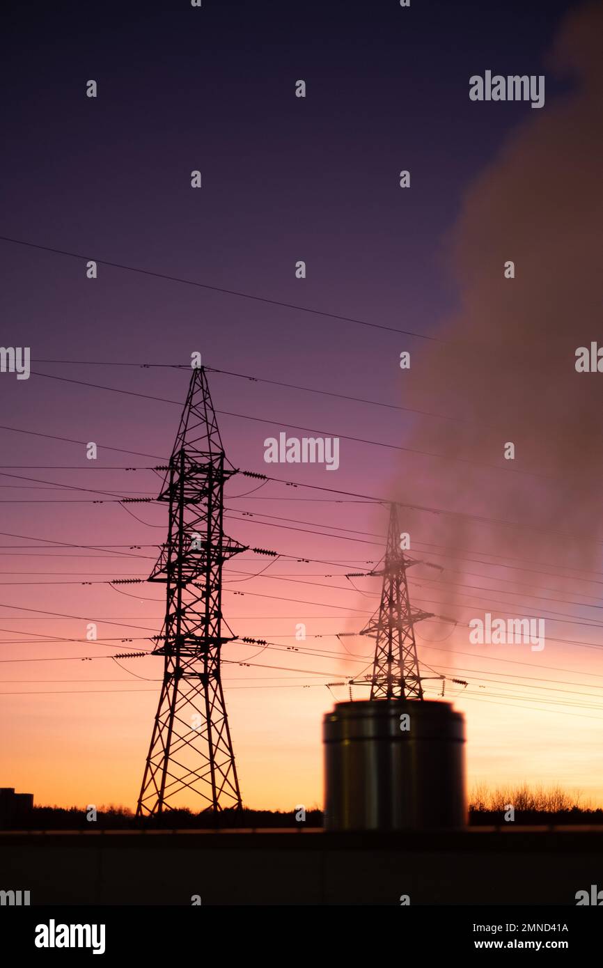 Stromnetz und Rauchschornstein am Sonnenuntergang. Turm und Leitungen. Hohe Strom- und Energiemarktpreise. Hohe Elektrizität und energetisch Stockfoto