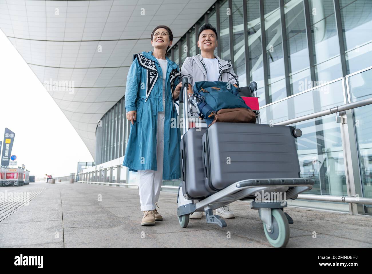 Glückliche ältere Paare, die am Flughafen ein Auto schieben Stockfoto