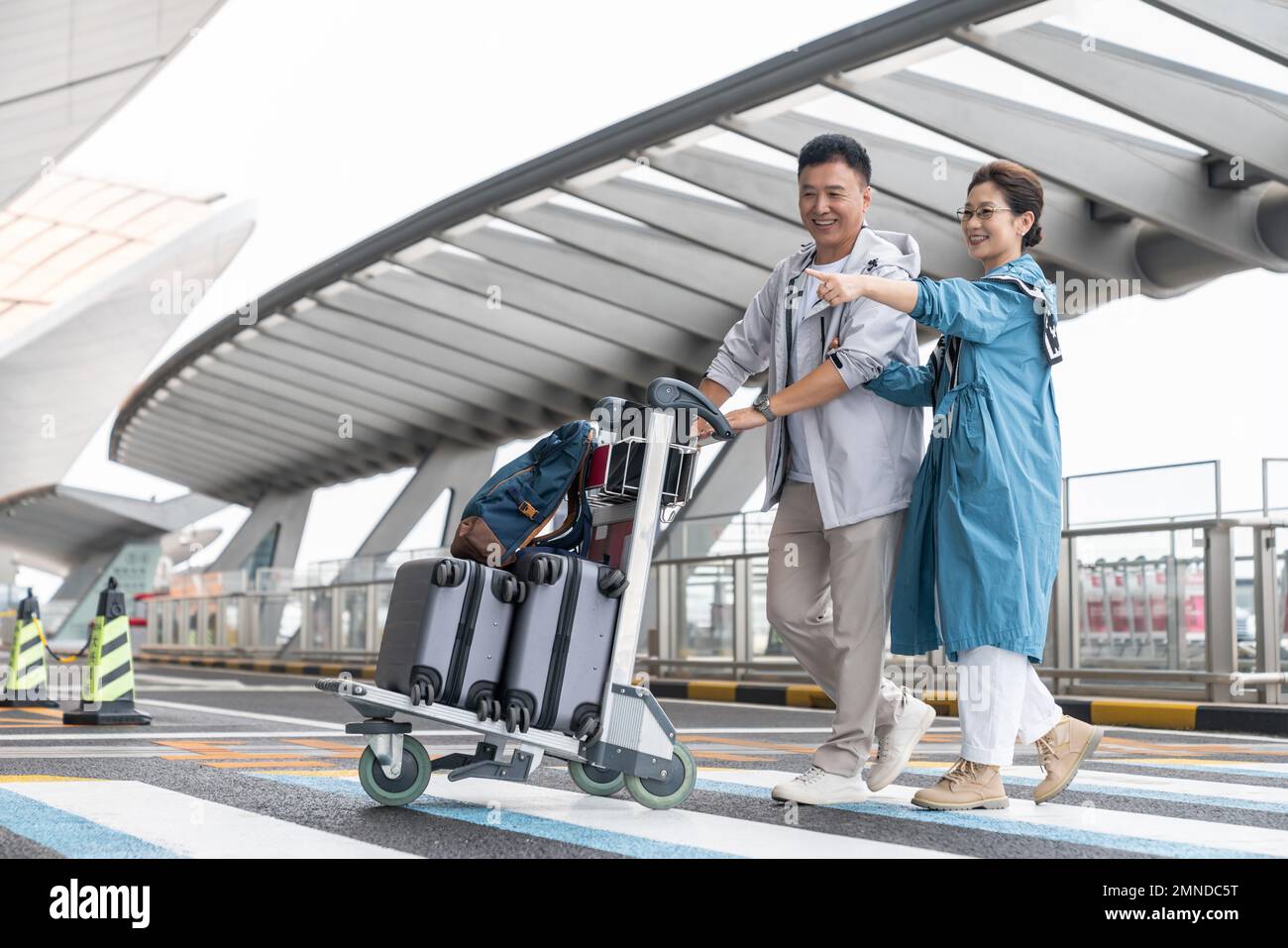 Glückliche ältere Paare, die am Flughafen ein Auto schieben Stockfoto