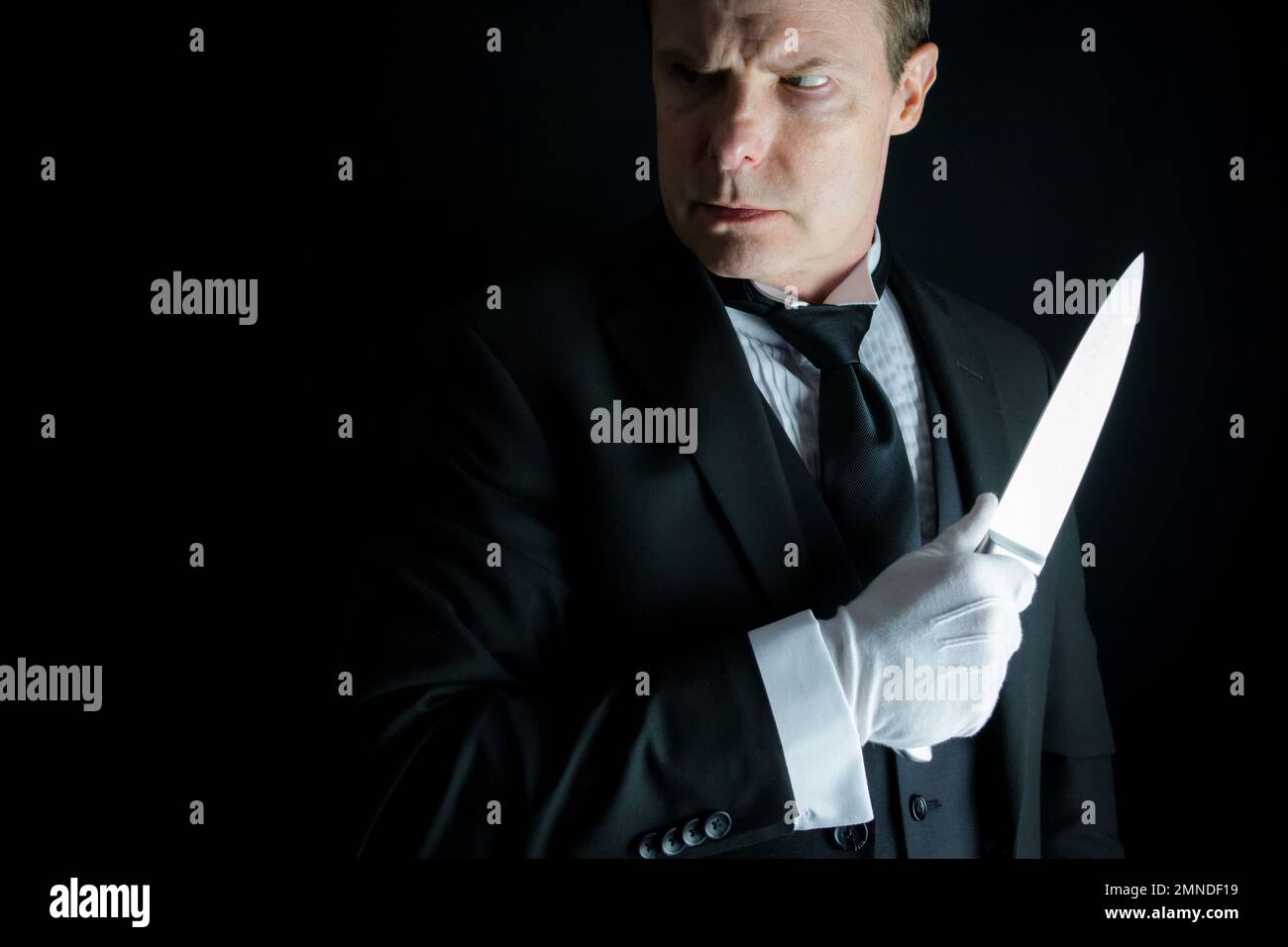 Butler in Dark – formeller Anzug und weiße Handschuhe mit scharfem Messer. Konzept von Butler Do IT. Klassisches Mordgeheimnis. Stockfoto