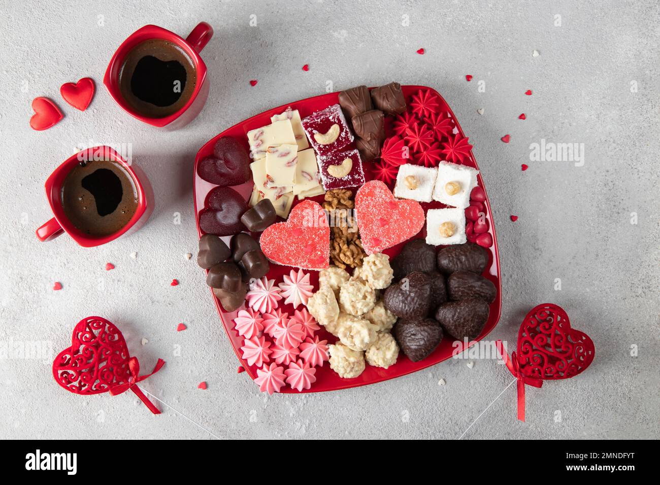 Süßer romantischer Teller mit Süßigkeiten, Schokolade, Nüssen, Baiser, türkischem Honig und Kaffee für zwei am Valentinstag auf grauem Hintergrund Stockfoto