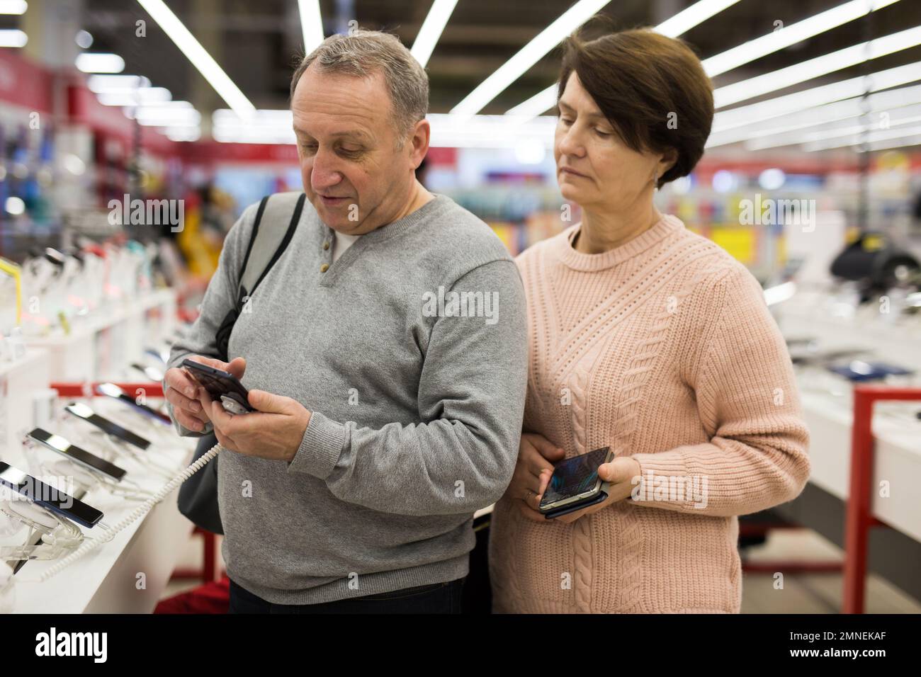 Ehefrau und Ehemann mittleren Alters pflücken neues Smartphone im Elektronikgeschäft Stockfoto