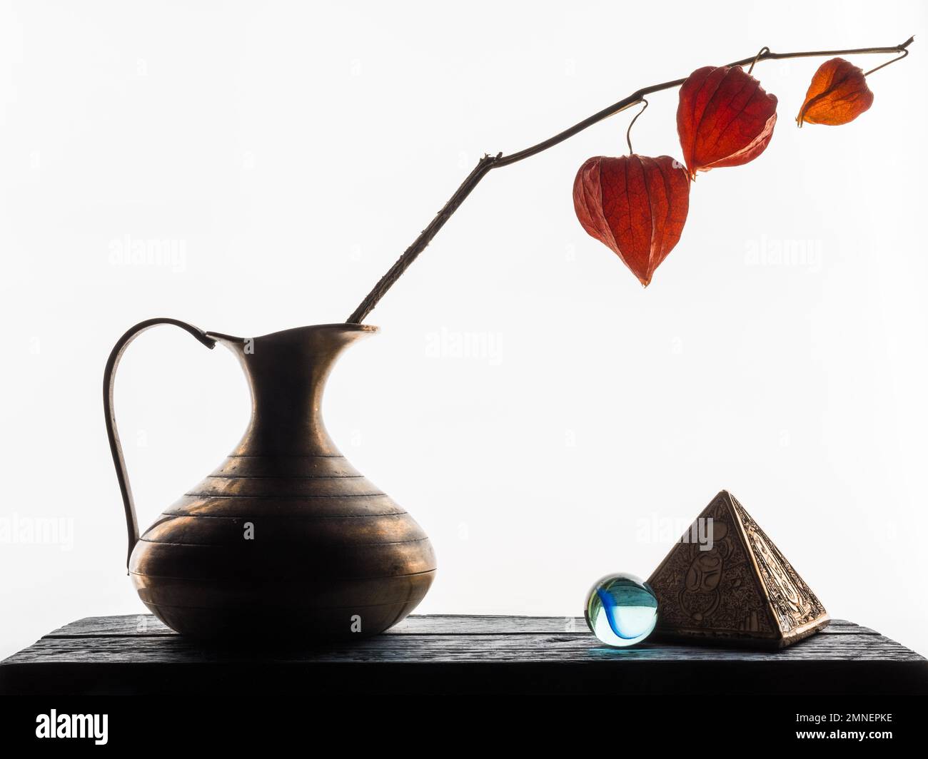 Stillleben mit vergoldeter Pyramide, Glaskugel und Physalis in Messingvase, Studioaufnahme, heller Hintergrund Stockfoto