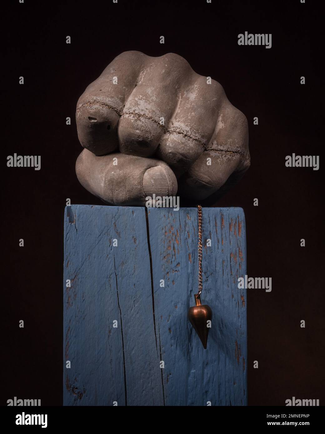 Stillleben mit Betonfaust Pendulum auf Holzblock, Studioaufnahme, dunkler Hintergrund Stockfoto