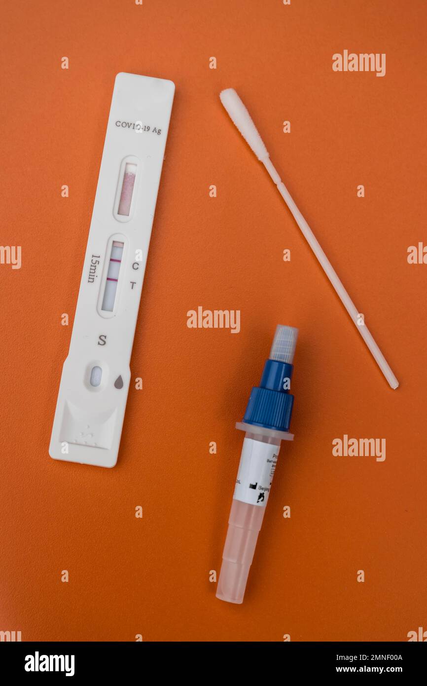 Testkassette, Tupfer und Testflüssigkeit, Covid-19-Antigen-Testkit, positives Testergebnis, Selbsttest, SARS-CoV-2, Corona-Virus, Pandemie, orangefarbener Hintergrund Stockfoto