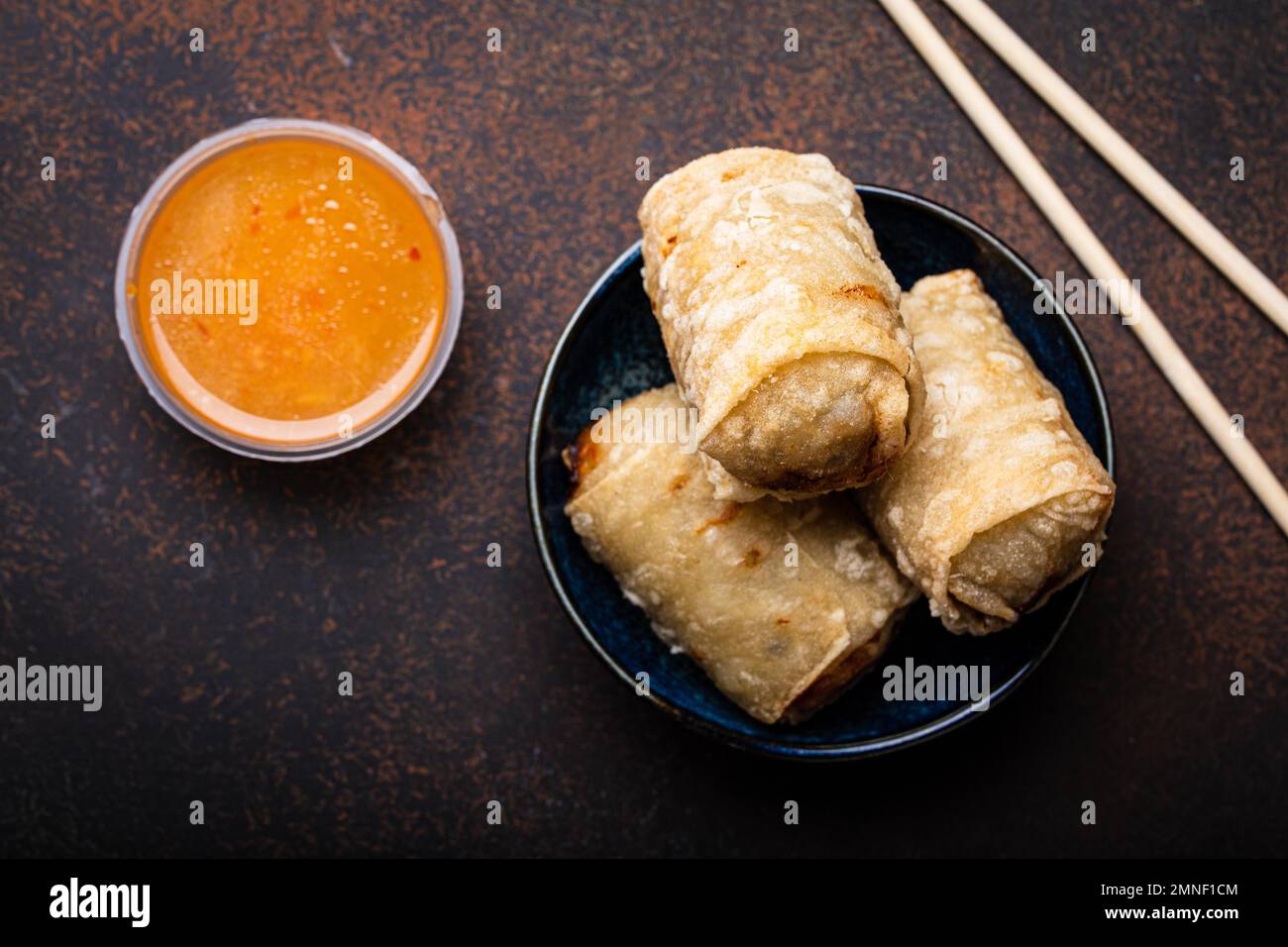 Chinesisches, thailändisches oder vietnamesisches traditionelles Gericht, frittierte Frühlingsrollen mit Füllung auf dem Teller mit süßer saurer Sauce auf rustikalem Betonhintergrund Stockfoto