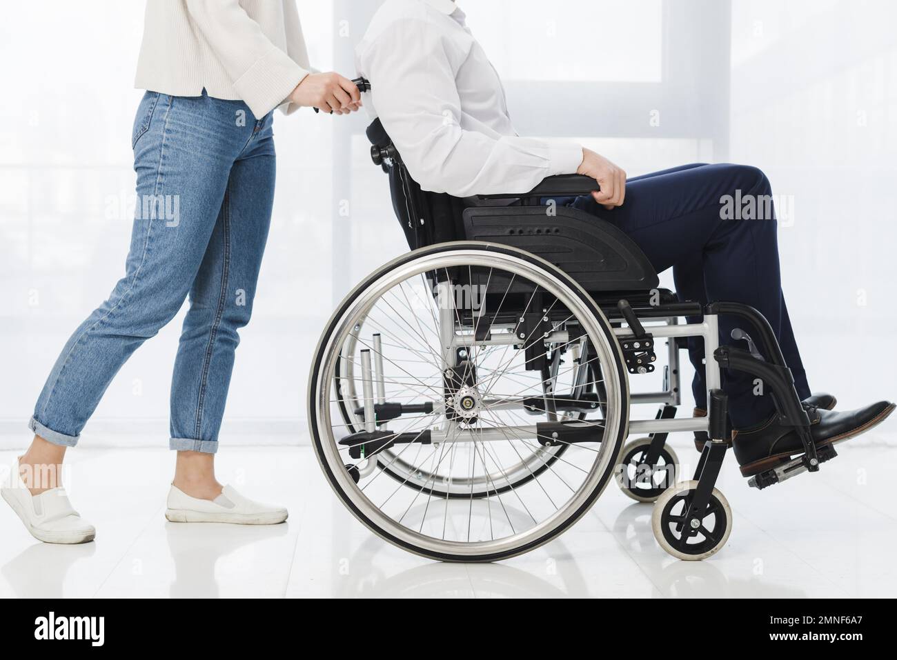 Eine Frau im unteren Bereich, die einen Mann schubst, der im Rollstuhl sitzt. Auflösung und hochwertige Fotos Stockfoto