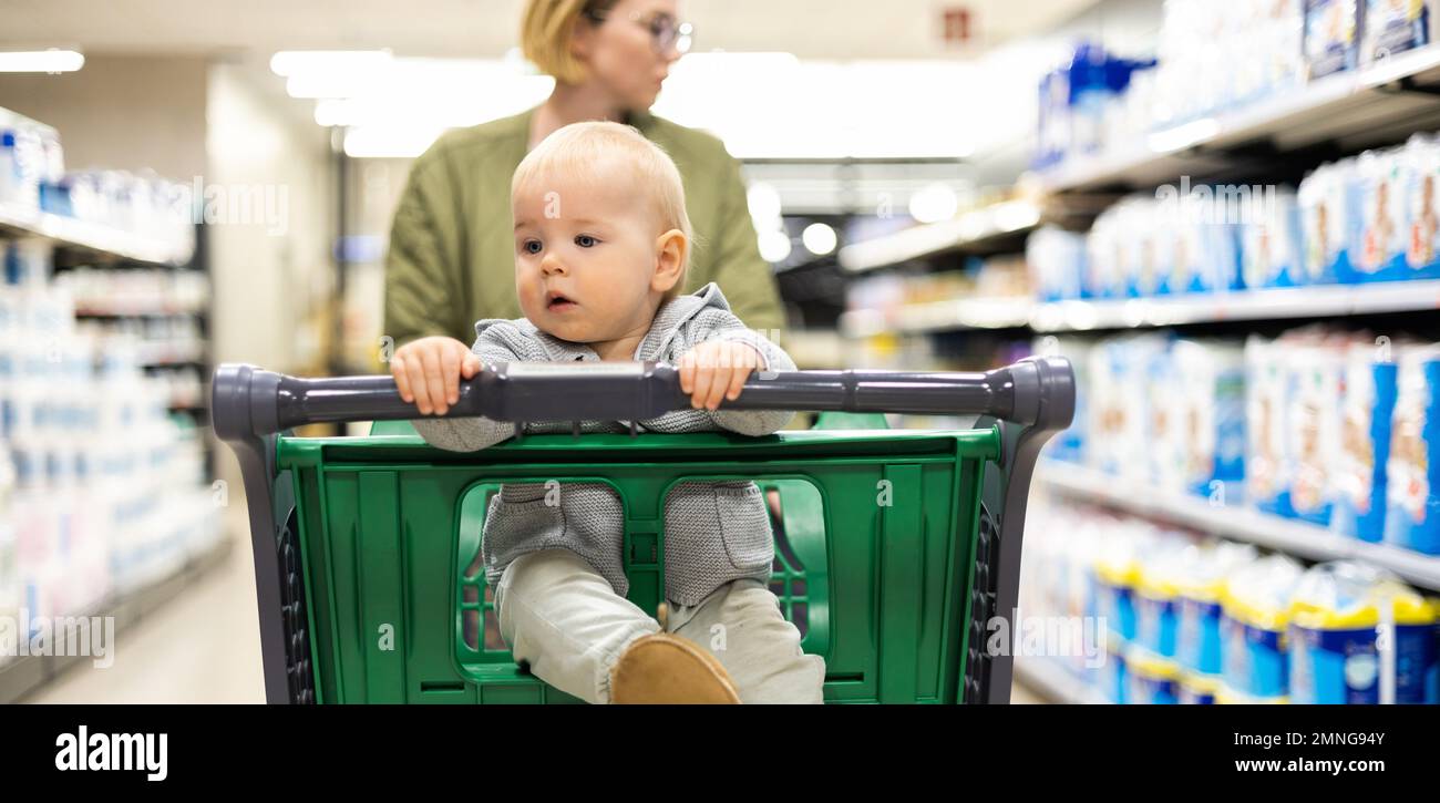 Mutter schiebt den Einkaufswagen mit ihrem kleinen Jungen durch die Abteilung im Supermarkt. Einkaufen mit Kindern Konzept Stockfoto