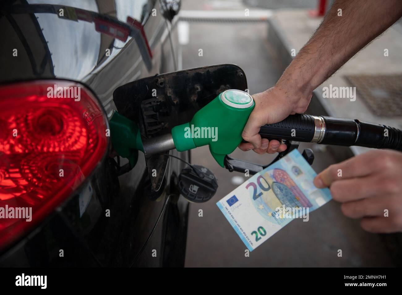 Hand eines Mannes, der das Auto betankt und eine 20-Euro-Banknote in der Hand hält, Konzept steigender Kraftstoffpreise Stockfoto