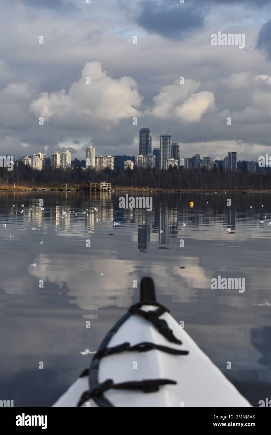 Ein Kajakfahrer eroberte die Stadt Burnaby, die sich an einem bedeckten Wintertag im ruhigen Wasser des Burnaby Lake widerspiegelt. Stockfoto