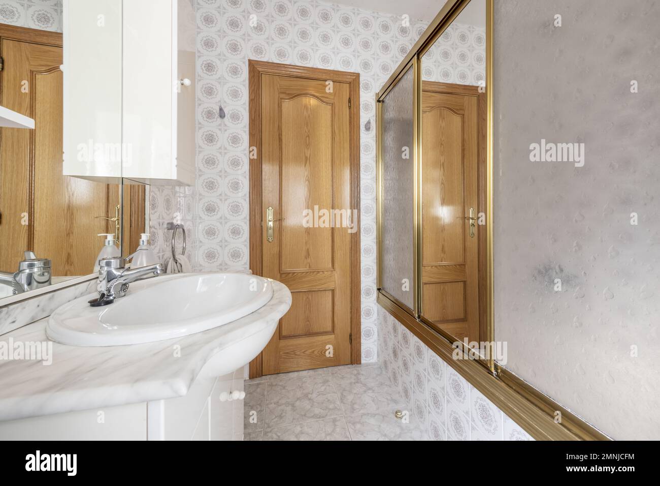 Toilette mit weißem Holzschrank mit Marmorablagefläche und Spiegel mit Schubladen, integrierten Lampen und Duschkabine mit Schiebewänden Stockfoto
