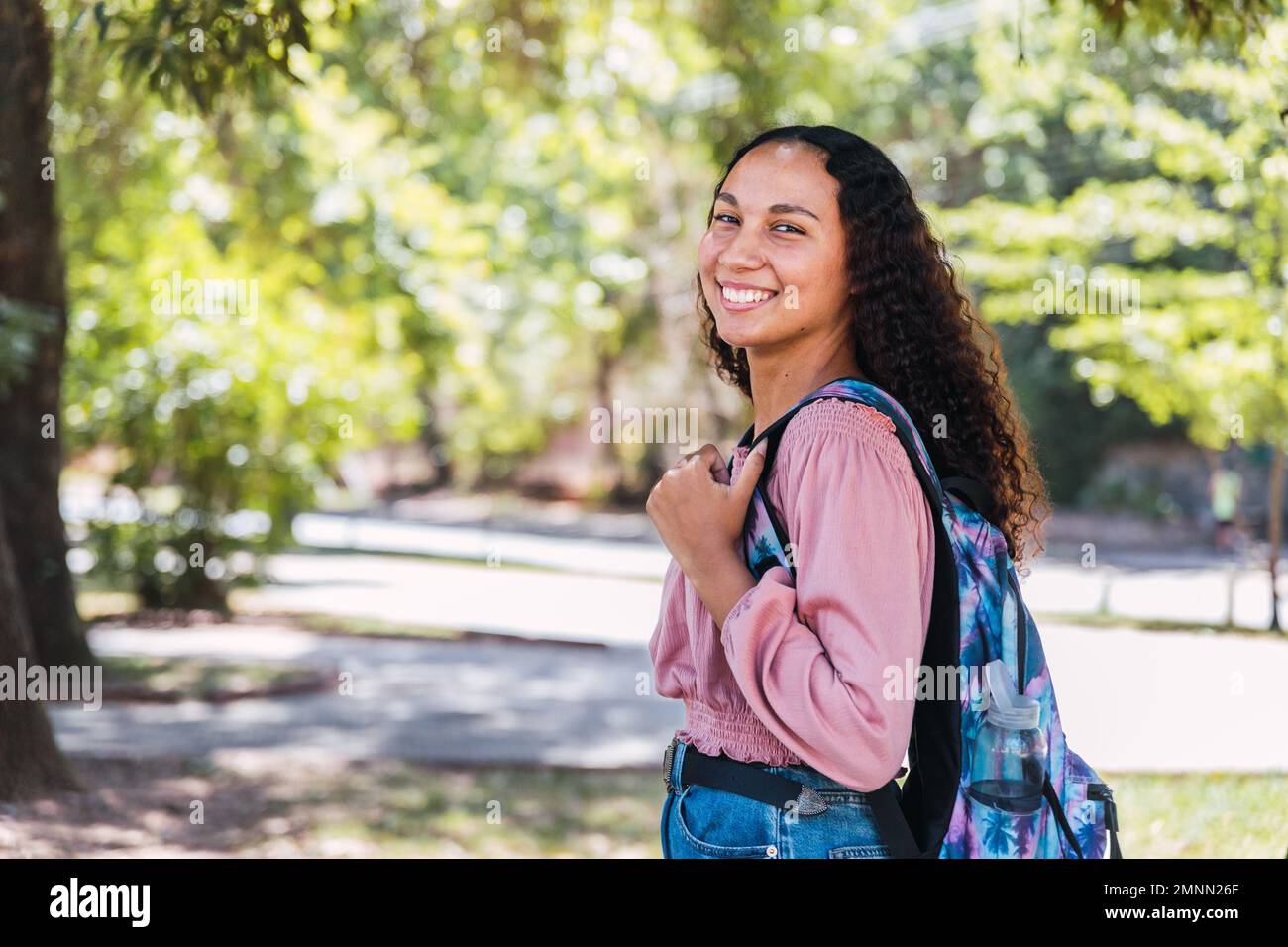 Erfolgreiche lateinische Studentin, die im Park lächelt. Postsekundärer Unterricht. Stockfoto