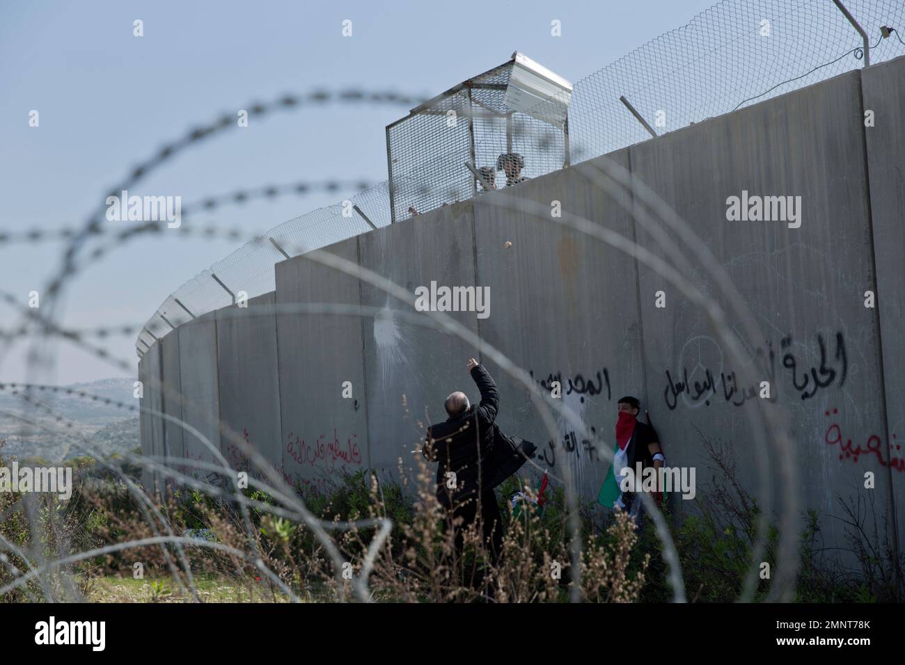 Palestinian protesters throw stones toward Israeli Border Policemen in a guard tower behind a section of the Israeli separation barrier, during a protest in the West Bank village of Bil'in, west of Ramallah, Friday, March 2, 2018. Palestinian protesters and foreign activists marched to commemorate the 13th anniversary of the ongoing weekly protests against the Israeli separation barrier and settlements in Bil'in. (AP Photo/Nasser Nasser) Stockfoto